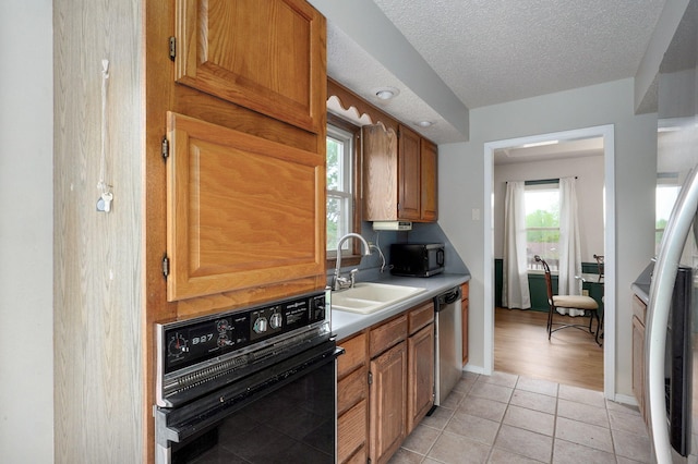 523 E Camino St, Springfield, MO 65810 - kitchen featuring brown cabinetry, a textured ceiling, a sink, light tile patterned floors, and stainless steel appliances