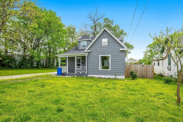 rear view of house with fence, covered porch, a shingled roof, and a lawn