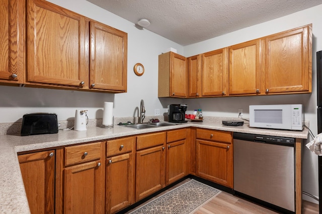 kitchen featuring white microwave, light countertops, a sink, light wood-style flooring, and dishwasher