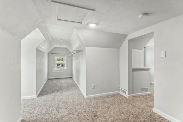 additional living space featuring attic access, visible vents, vaulted ceiling, baseboards, and carpet