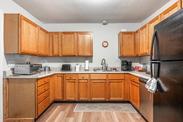 kitchen with stainless steel dishwasher, freestanding refrigerator, light countertops, a sink, and light wood-style flooring