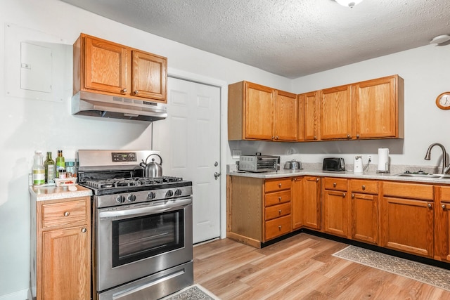 kitchen featuring stainless steel range with gas stovetop, a sink, light countertops, light wood finished floors, and under cabinet range hood