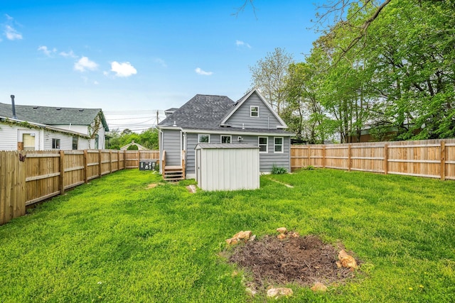 exterior space with a storage unit, a fenced backyard, an outbuilding, and a shingled roof