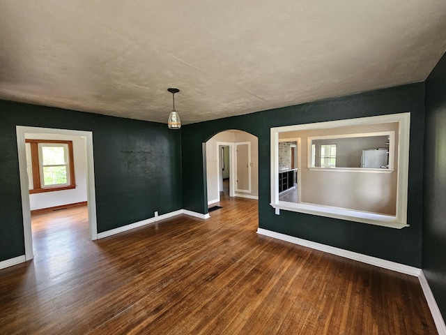 unfurnished room with arched walkways, baseboards, and wood finished floors