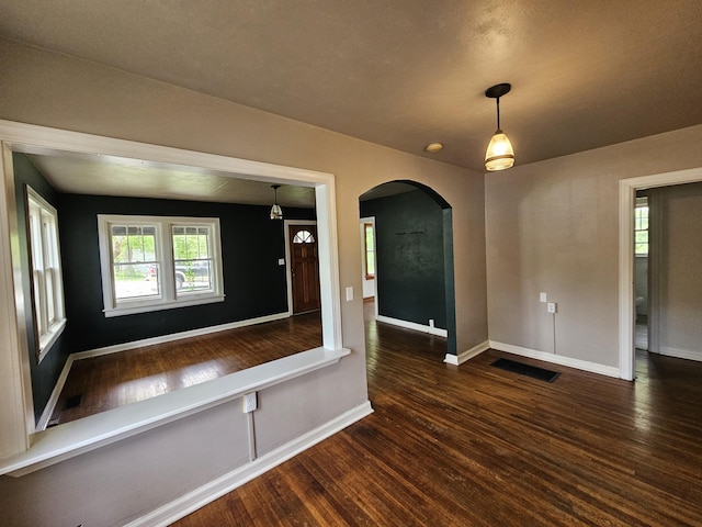 unfurnished room featuring arched walkways, baseboards, dark wood-style flooring, and visible vents