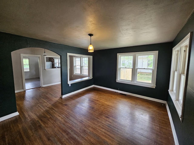 unfurnished dining area with baseboards, arched walkways, and dark wood-style floors