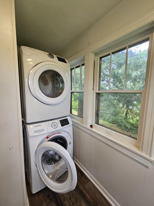 clothes washing area with dark wood-type flooring, laundry area, a decorative wall, and stacked washer / dryer