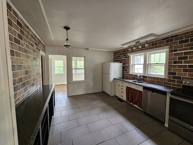 kitchen featuring brick wall, dark countertops, a sink, hanging light fixtures, and stainless steel appliances