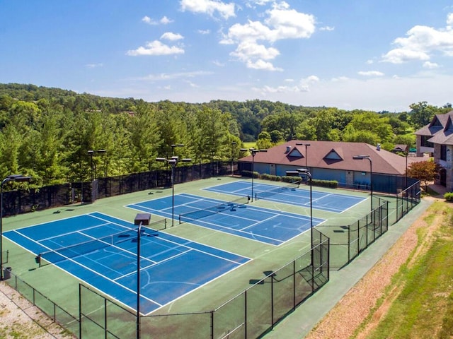 view of tennis court featuring fence, community basketball court, and a forest view