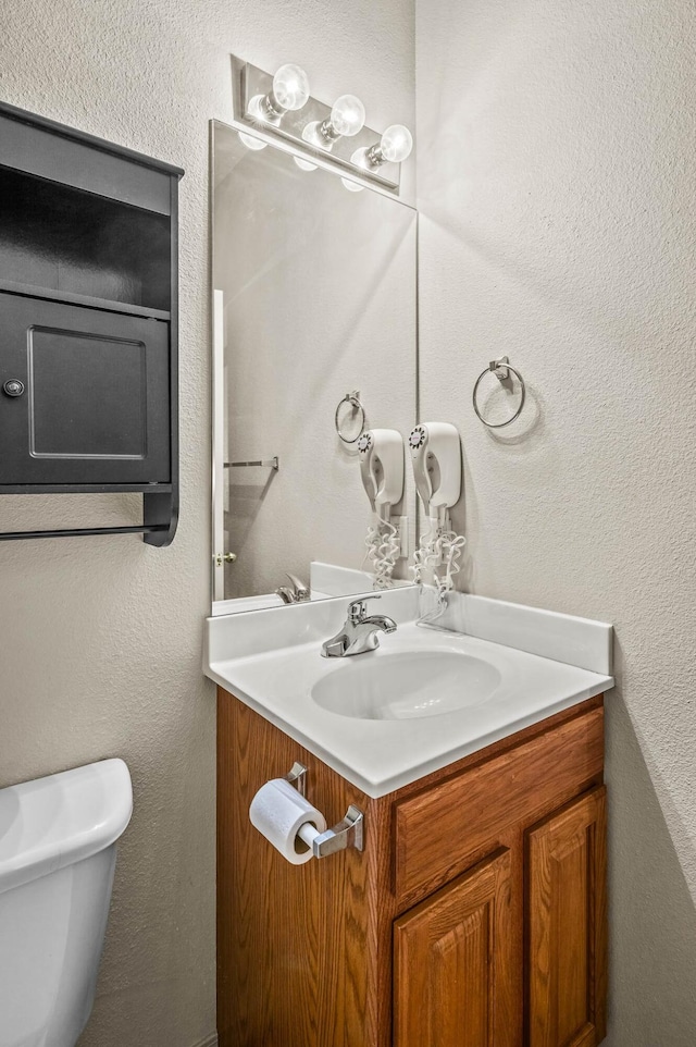 half bath featuring vanity, a textured wall, and toilet