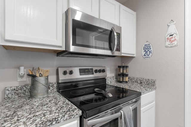 kitchen featuring appliances with stainless steel finishes, light stone counters, a textured wall, and white cabinetry