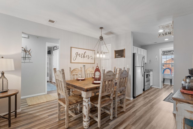 dining room featuring light wood-type flooring, baseboards, a chandelier, and visible vents