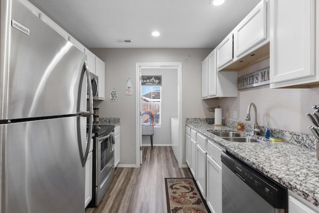 kitchen with visible vents, wood finished floors, white cabinets, a sink, and appliances with stainless steel finishes