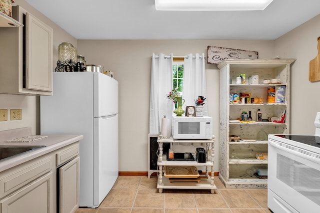 kitchen with light tile patterned flooring, a sink, white appliances, light countertops, and baseboards