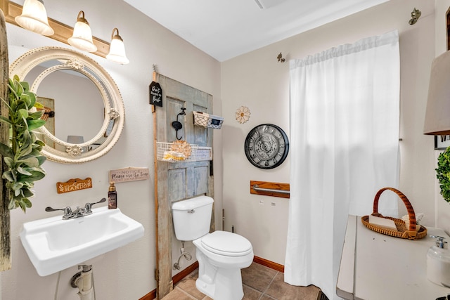 bathroom with toilet, baseboards, a sink, and tile patterned flooring