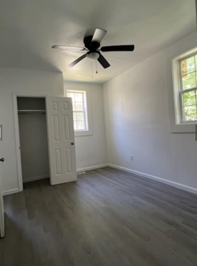 unfurnished bedroom with baseboards, multiple windows, and dark wood-type flooring