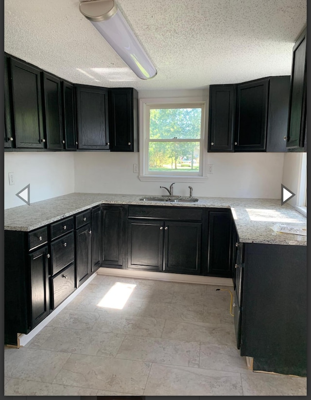 kitchen with dark cabinets, a textured ceiling, light stone countertops, and a sink