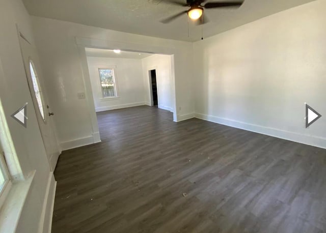empty room featuring baseboards, ceiling fan, and dark wood-type flooring