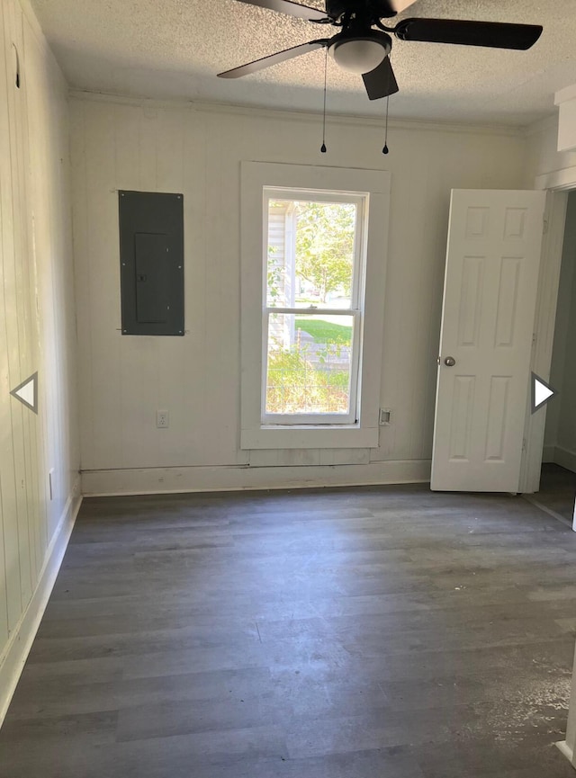 empty room with ceiling fan, electric panel, a textured ceiling, and wood finished floors