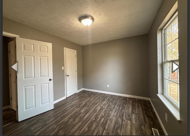 unfurnished bedroom featuring a textured ceiling, baseboards, dark wood finished floors, and visible vents