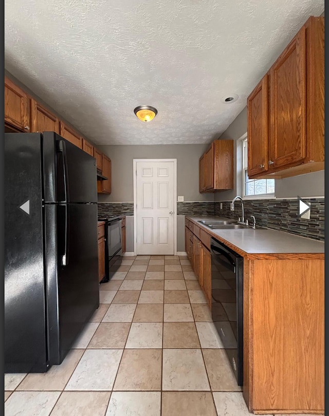 kitchen with brown cabinets, a sink, tasteful backsplash, under cabinet range hood, and black appliances
