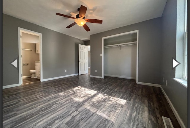 unfurnished bedroom featuring baseboards, ensuite bathroom, a closet, and dark wood finished floors