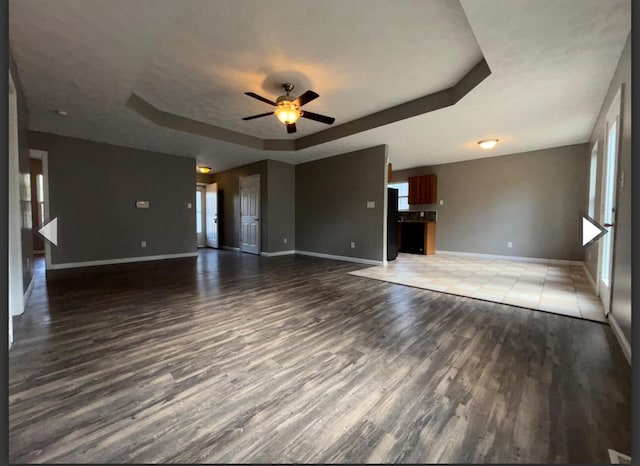 unfurnished living room featuring light wood-style floors, a ceiling fan, baseboards, and a tray ceiling