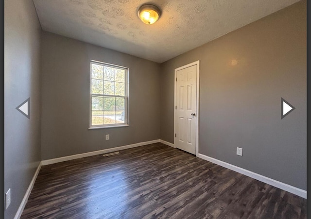 empty room with dark wood-style flooring, baseboards, visible vents, and a textured ceiling