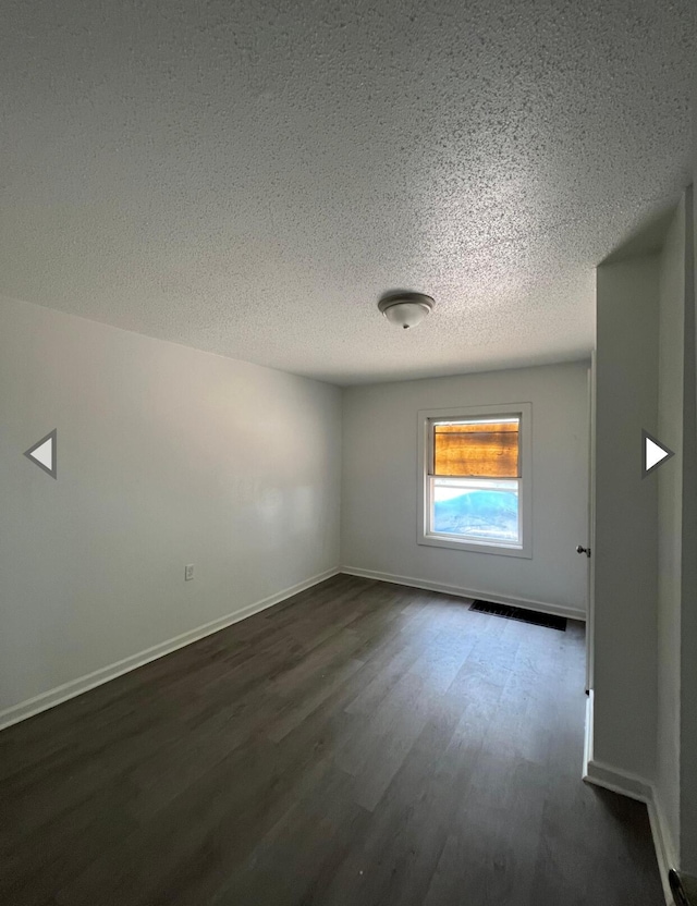 spare room with baseboards, a textured ceiling, and dark wood finished floors