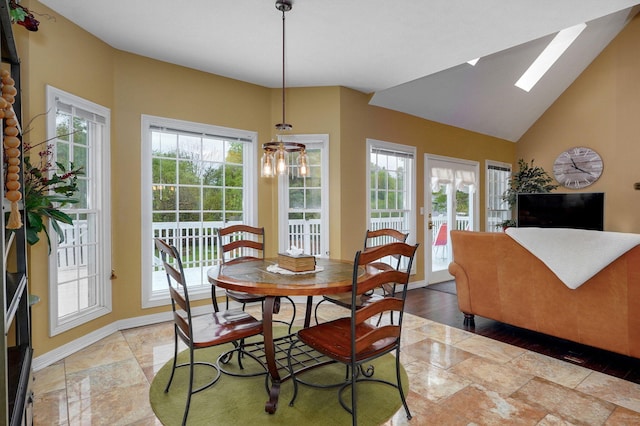 dining space with baseboards, stone finish flooring, and lofted ceiling with skylight
