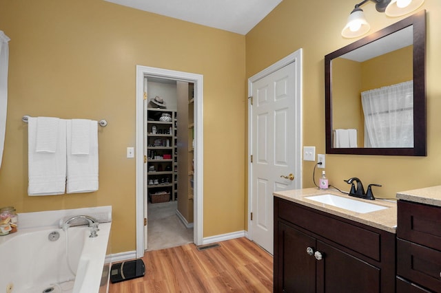 bathroom featuring vanity, baseboards, a tub with jets, and wood finished floors