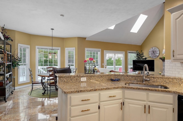 kitchen featuring light stone countertops, a sink, a peninsula, tasteful backsplash, and a skylight