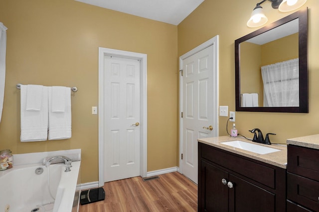 full bath with vanity, baseboards, a tub with jets, and wood finished floors