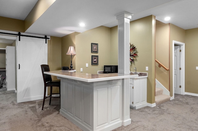 interior space featuring a kitchen breakfast bar, light colored carpet, a barn door, a peninsula, and white cabinetry