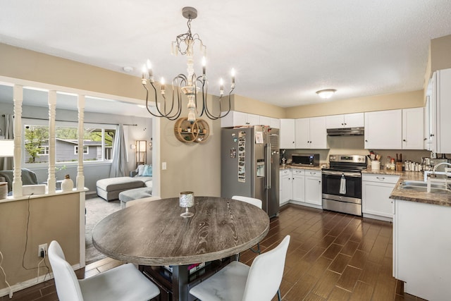 kitchen featuring wood finish floors, white cabinetry, under cabinet range hood, a sink, and stainless steel appliances