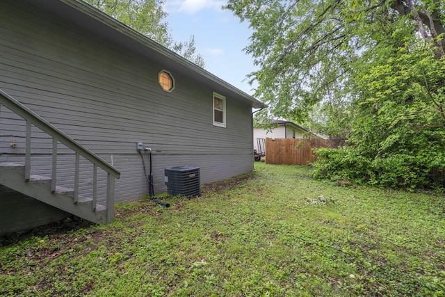 view of side of home featuring a lawn, central AC, and fence