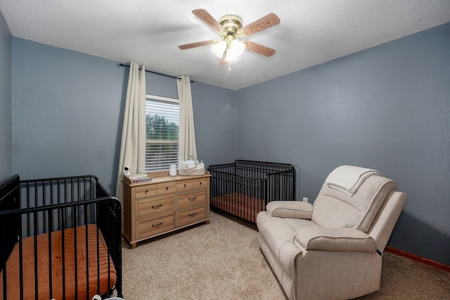 bedroom with baseboards, a ceiling fan, a nursery area, and light carpet