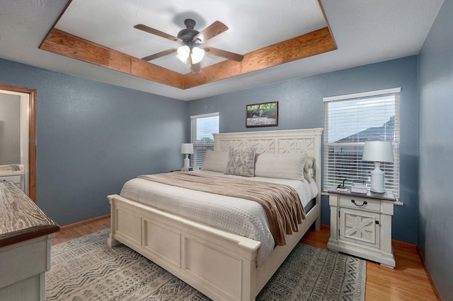 bedroom featuring a raised ceiling, baseboards, a ceiling fan, and light wood-style flooring