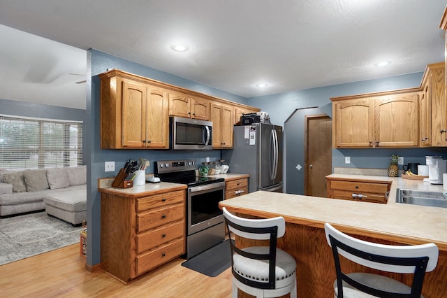 kitchen with light countertops, light wood finished floors, a peninsula, and stainless steel appliances