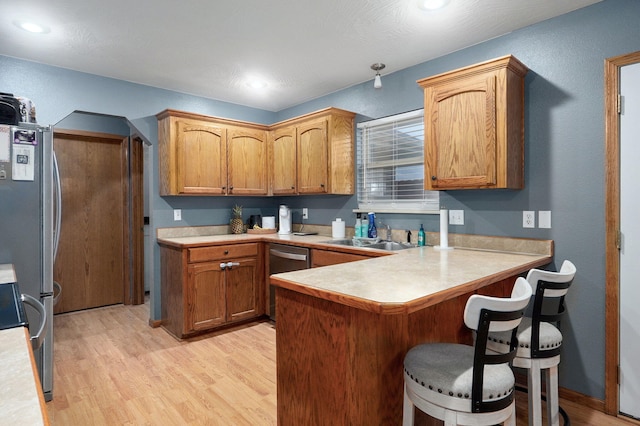 kitchen with light countertops, a peninsula, appliances with stainless steel finishes, and light wood-type flooring