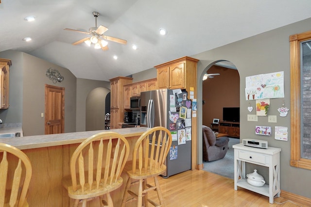 kitchen featuring ceiling fan, a breakfast bar area, arched walkways, stainless steel appliances, and light wood-style flooring