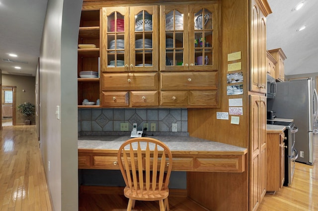 kitchen with brown cabinetry, backsplash, appliances with stainless steel finishes, light wood-type flooring, and light countertops