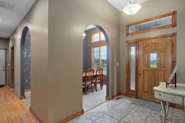 foyer with baseboards, arched walkways, a towering ceiling, and visible vents