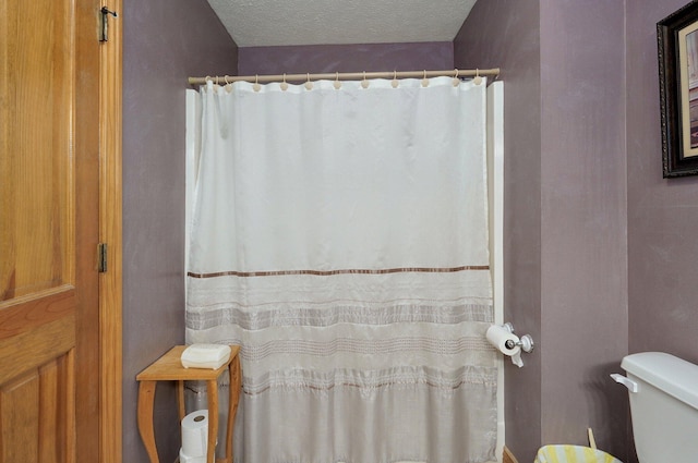 bathroom with a textured ceiling, toilet, and curtained shower