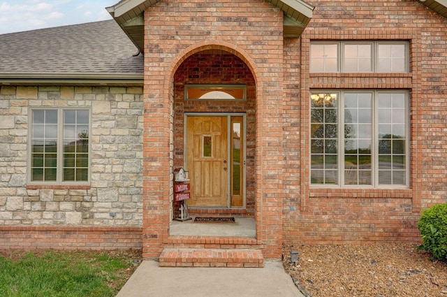 doorway to property with brick siding and a shingled roof