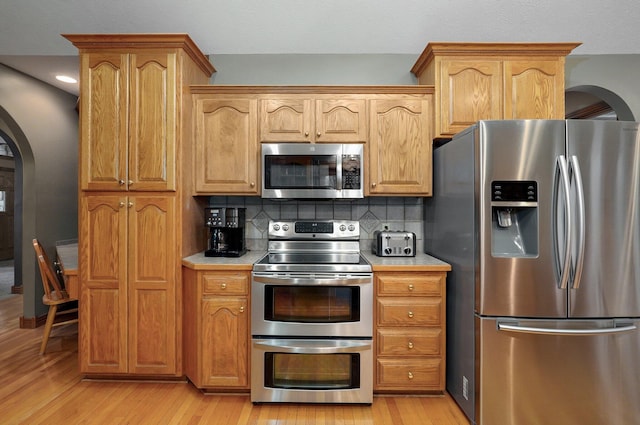 kitchen with appliances with stainless steel finishes, tasteful backsplash, arched walkways, light countertops, and light wood-style flooring