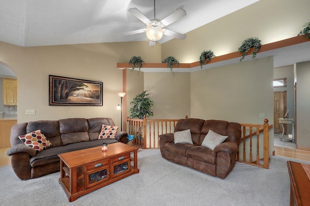 living area with arched walkways, ceiling fan, vaulted ceiling, and light carpet