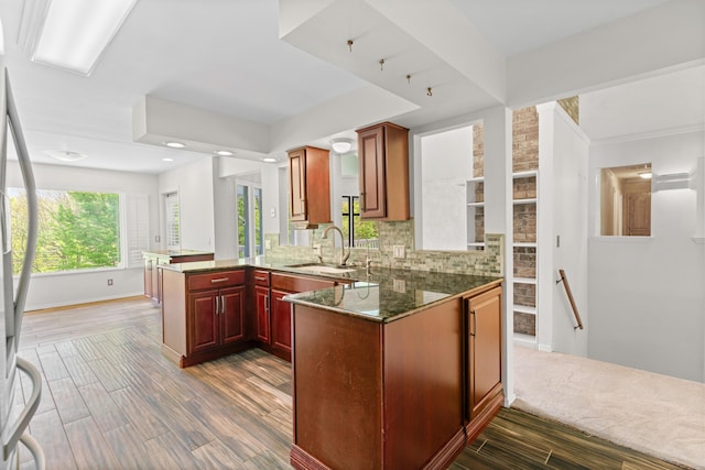 kitchen featuring backsplash, dark wood-style flooring, a sink, a peninsula, and stainless steel fridge