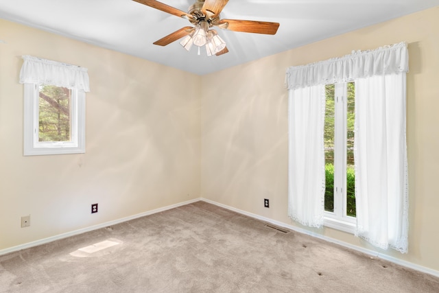 carpeted spare room featuring baseboards, visible vents, and ceiling fan