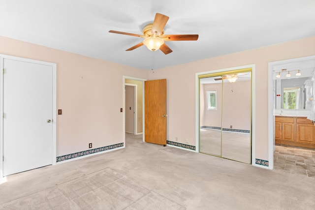 unfurnished bedroom featuring ensuite bathroom, light carpet, a closet, and ceiling fan